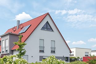 Ein modernes zweistöckiges Haus mit einem roten Satteldach, weißen Wänden und einem großen Dreiecksfenster im Dachgeschoss.